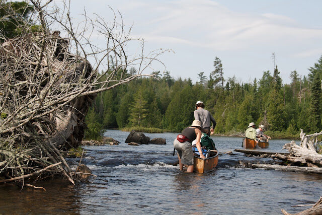 A trip group working canoes through a boulder-strewn rapids together