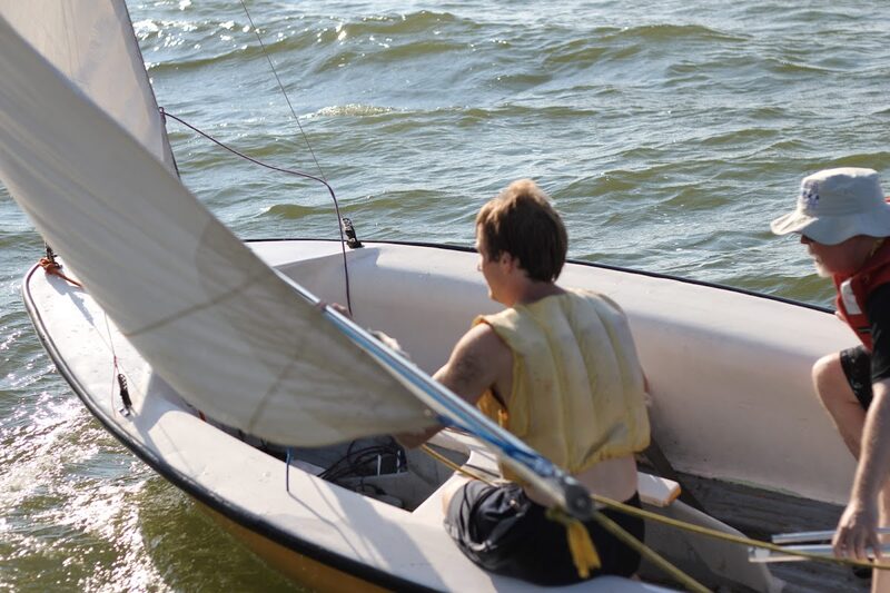 Two crew working the sail as water sprays off the bow of a 420
