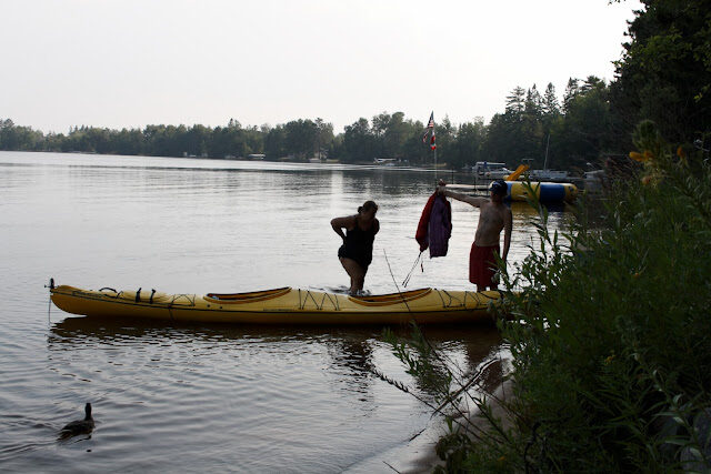 Two paddlers wading a tandem kayak out beside the dock, flag flying above